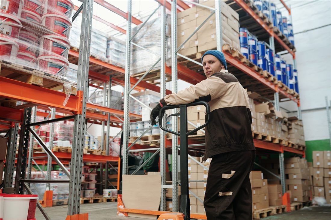 Warehouse worker operating a pallet jack among stacked goods